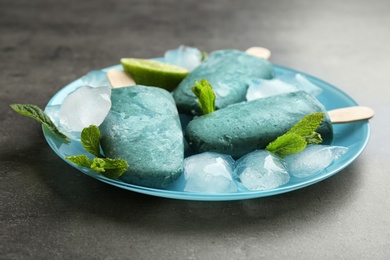 Photo of Plate with delicious spirulina popsicles and lime on grey background, closeup