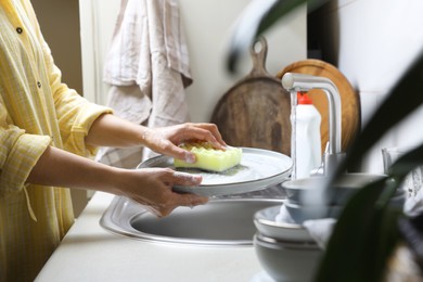 Photo of Woman washing plate in kitchen sink, closeup