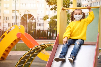 Little girl with medical face mask on playground during covid-19 quarantine