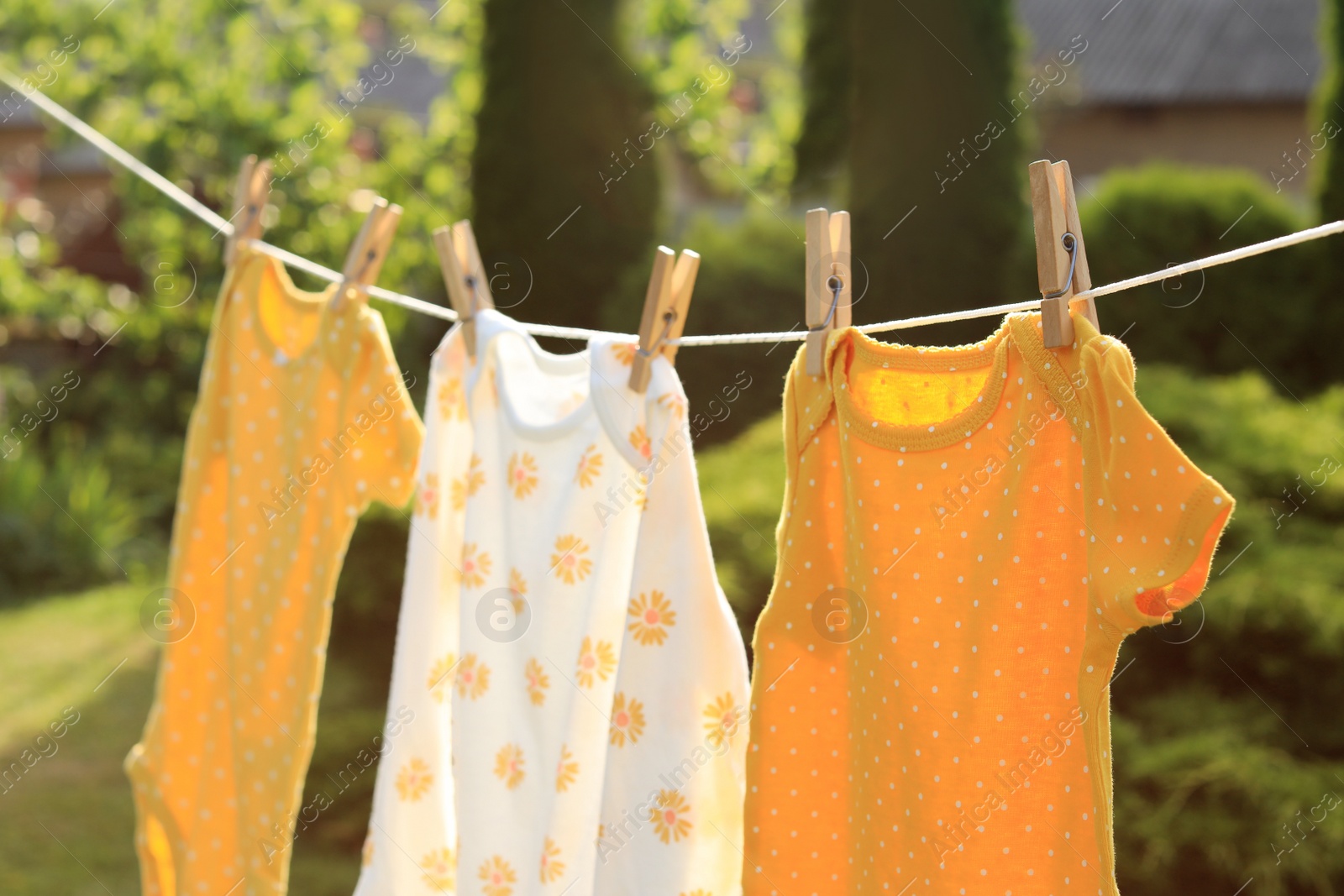 Photo of Clean baby onesies hanging on washing line in garden. Drying clothes