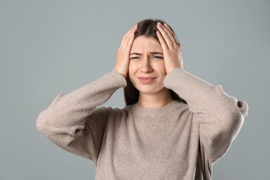 Young woman suffering from migraine on grey background