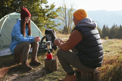 Young couple drinking coffee near camping tents in mountains