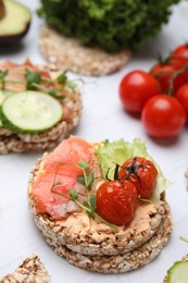 Photo of Crunchy buckwheat cakes with salmon, tomatoes and greens on white table, closeup