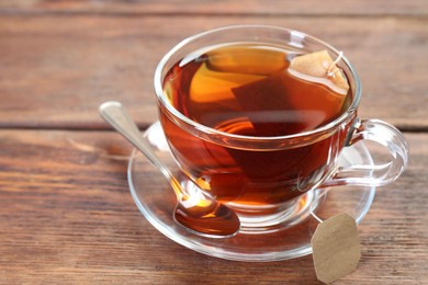 Photo of Brewing aromatic tea. Cup with teabag and spoon on wooden table