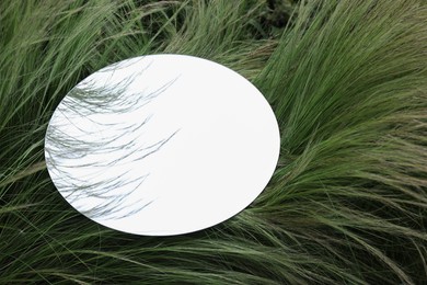 Photo of Round mirror on green grass reflecting sky. Space for text