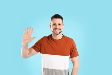 Photo of Cheerful man waving to say hello on light blue background