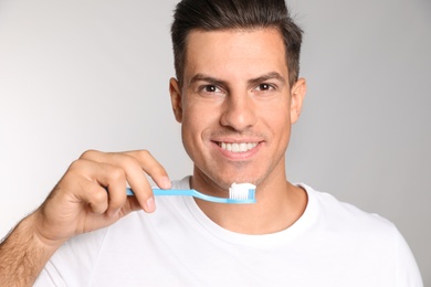Photo of Man holding toothbrush with paste on light background