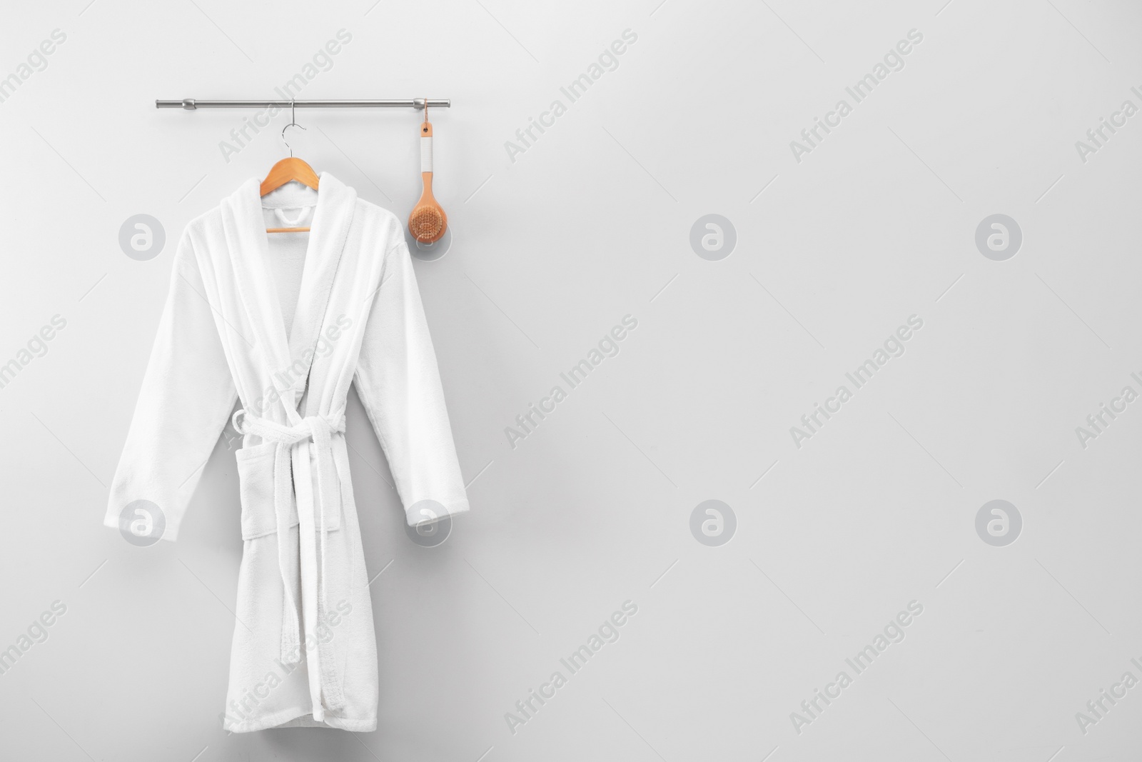 Photo of Hanger with clean bathrobe and brush on light wall. Space for text