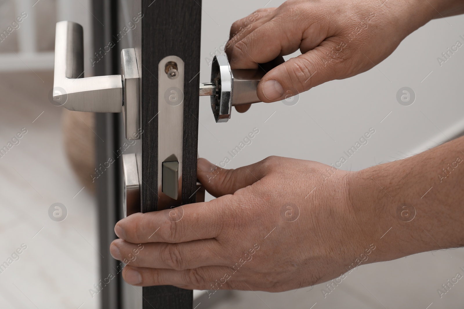 Photo of Handyman repairing door handle indoors, closeup view