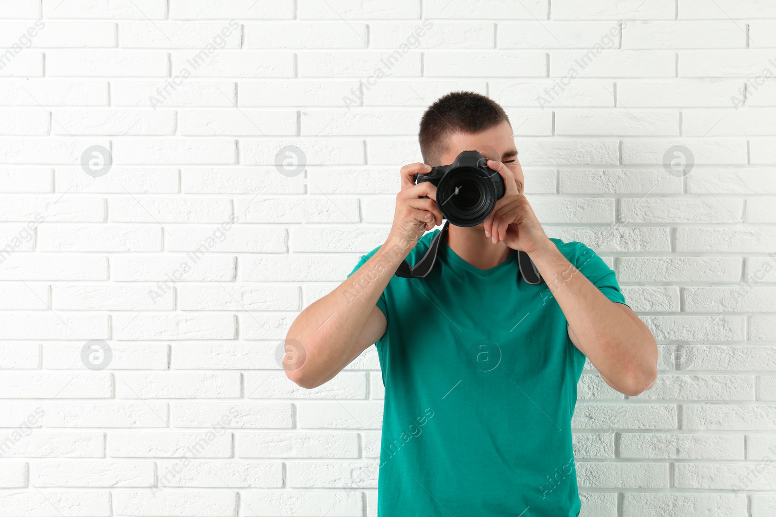 Photo of Young professional photographer taking picture near brick wall. Space for text