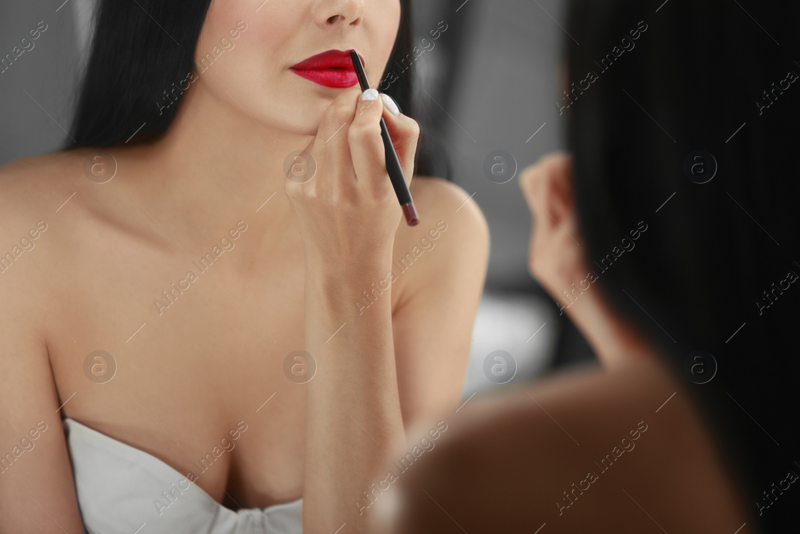 Photo of Young woman with beautiful makeup applying red lip pencil in front of mirror indoors, closeup