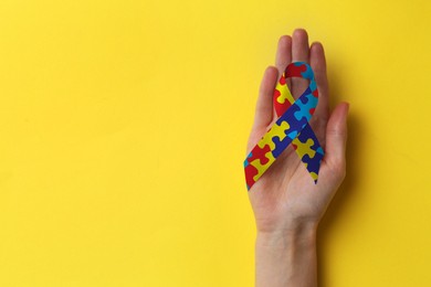 Image of World Autism Awareness Day. Woman with colorful puzzle ribbon on yellow background, top view with space for text
