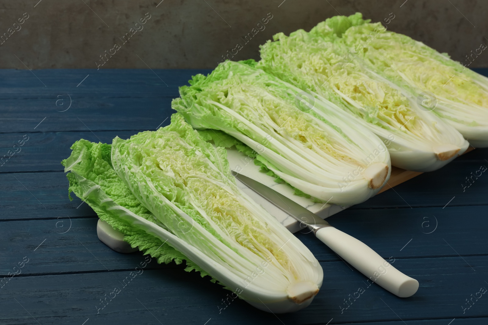 Photo of Cut fresh ripe Chinese cabbages on blue wooden table