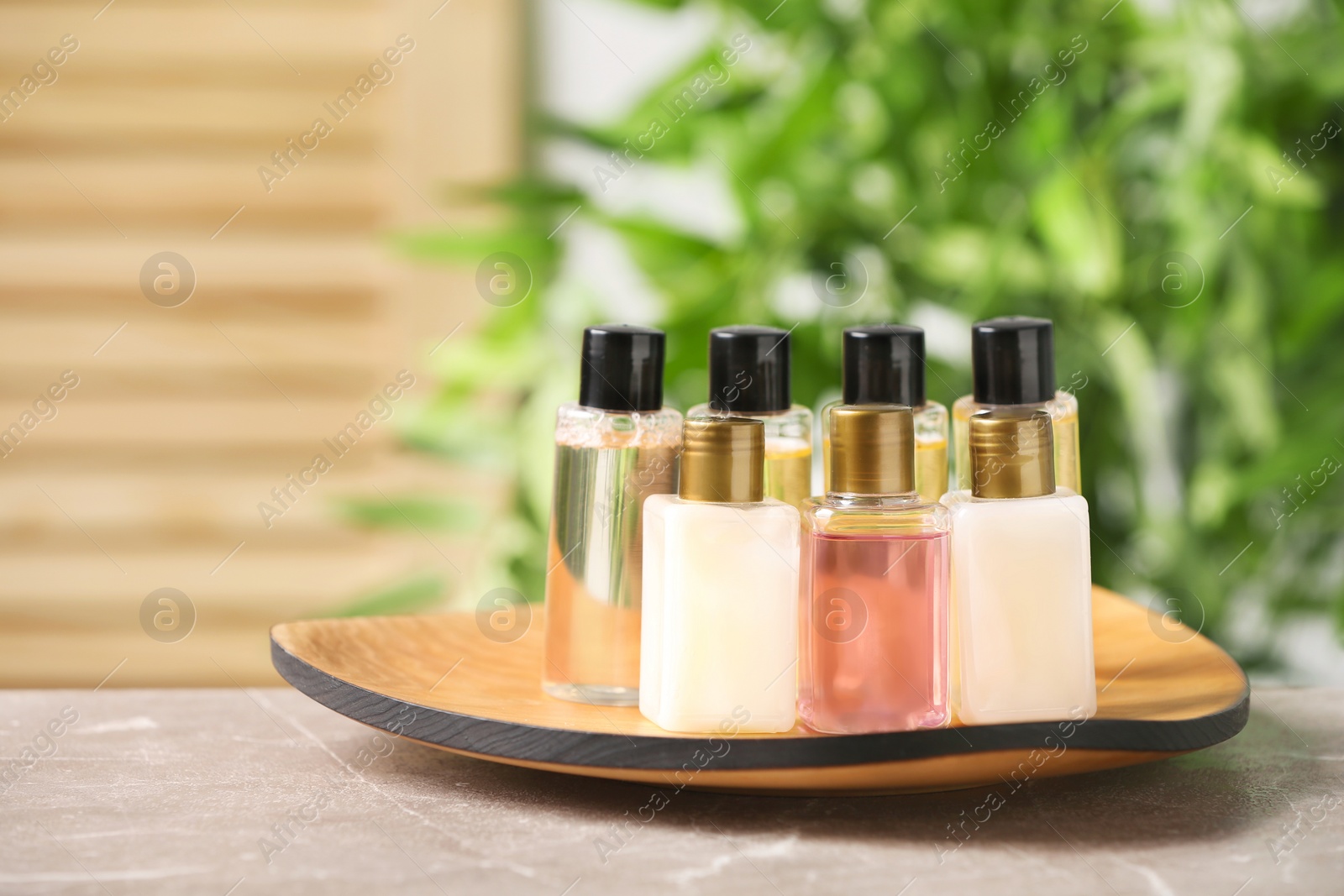 Photo of Mini bottles with cosmetic products on table against blurred background, space for text. Hotel amenities