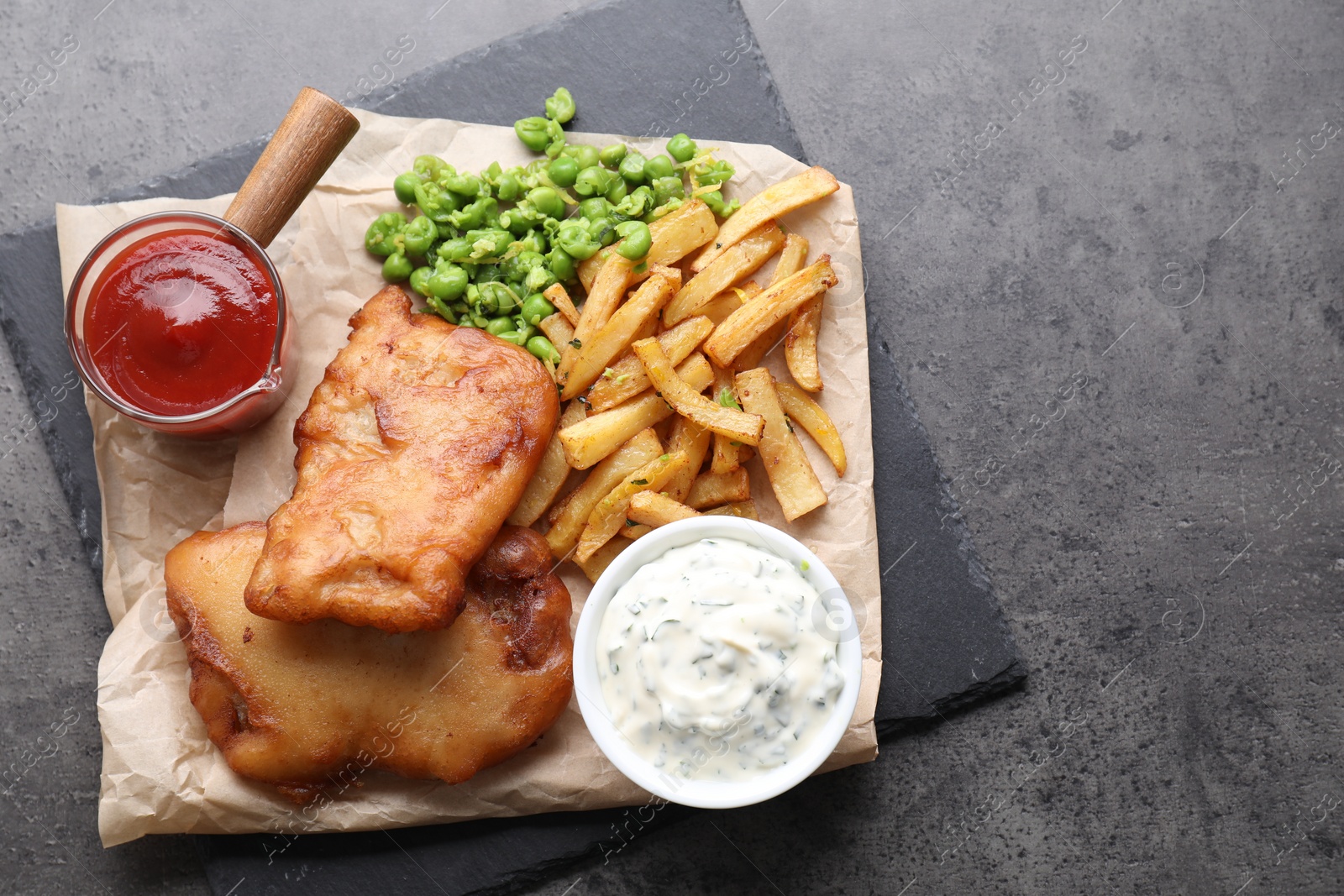 Photo of Tasty fish, chips, sauces and peas on grey table, top view. Space for text