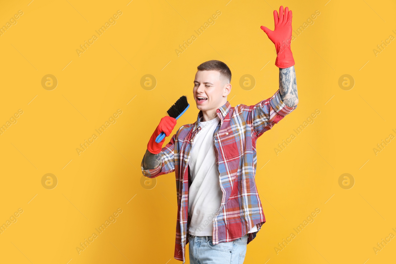 Photo of Handsome young man with brush singing on orange background