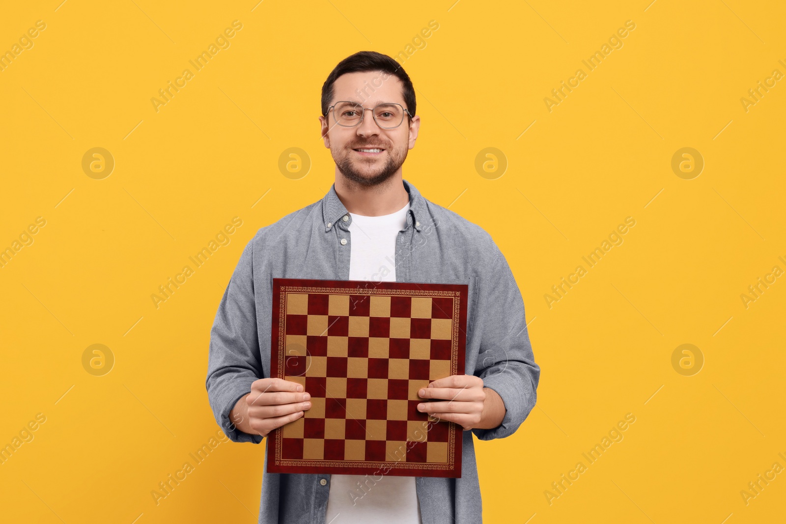 Photo of Handsome man holding chessboard on orange background