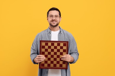 Photo of Handsome man holding chessboard on orange background