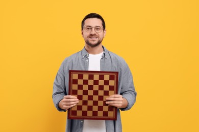 Handsome man holding chessboard on orange background