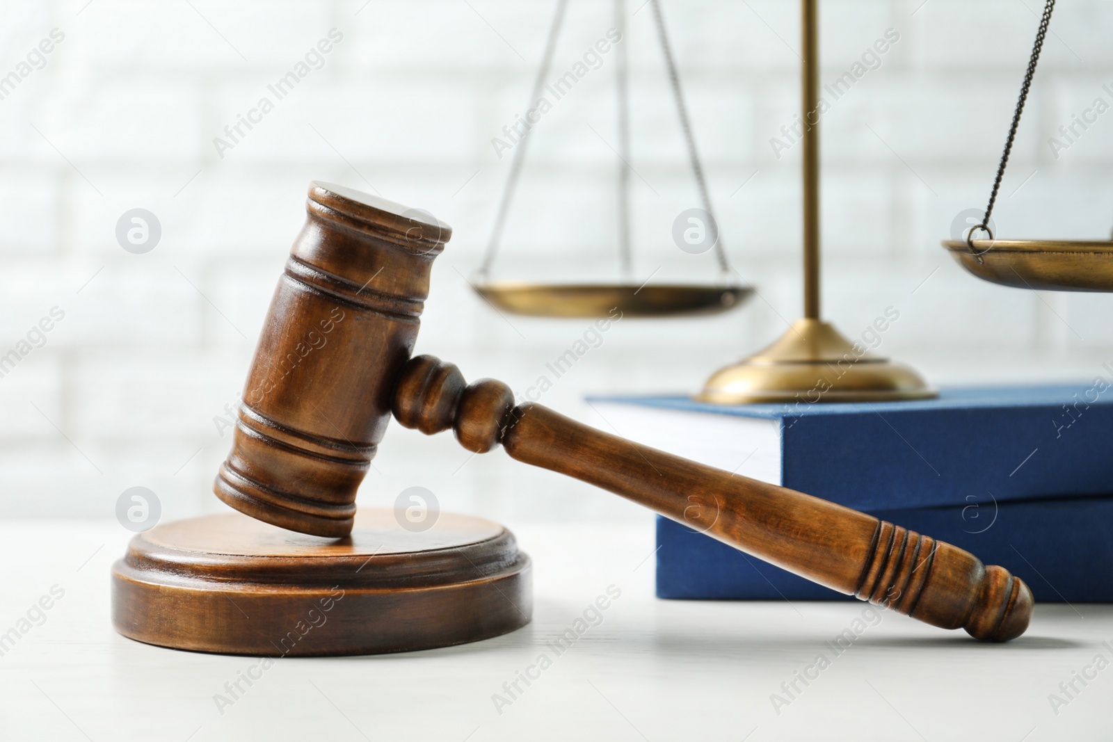 Photo of Wooden gavel, scales of justice and books on table against brick wall, closeup. Law concept