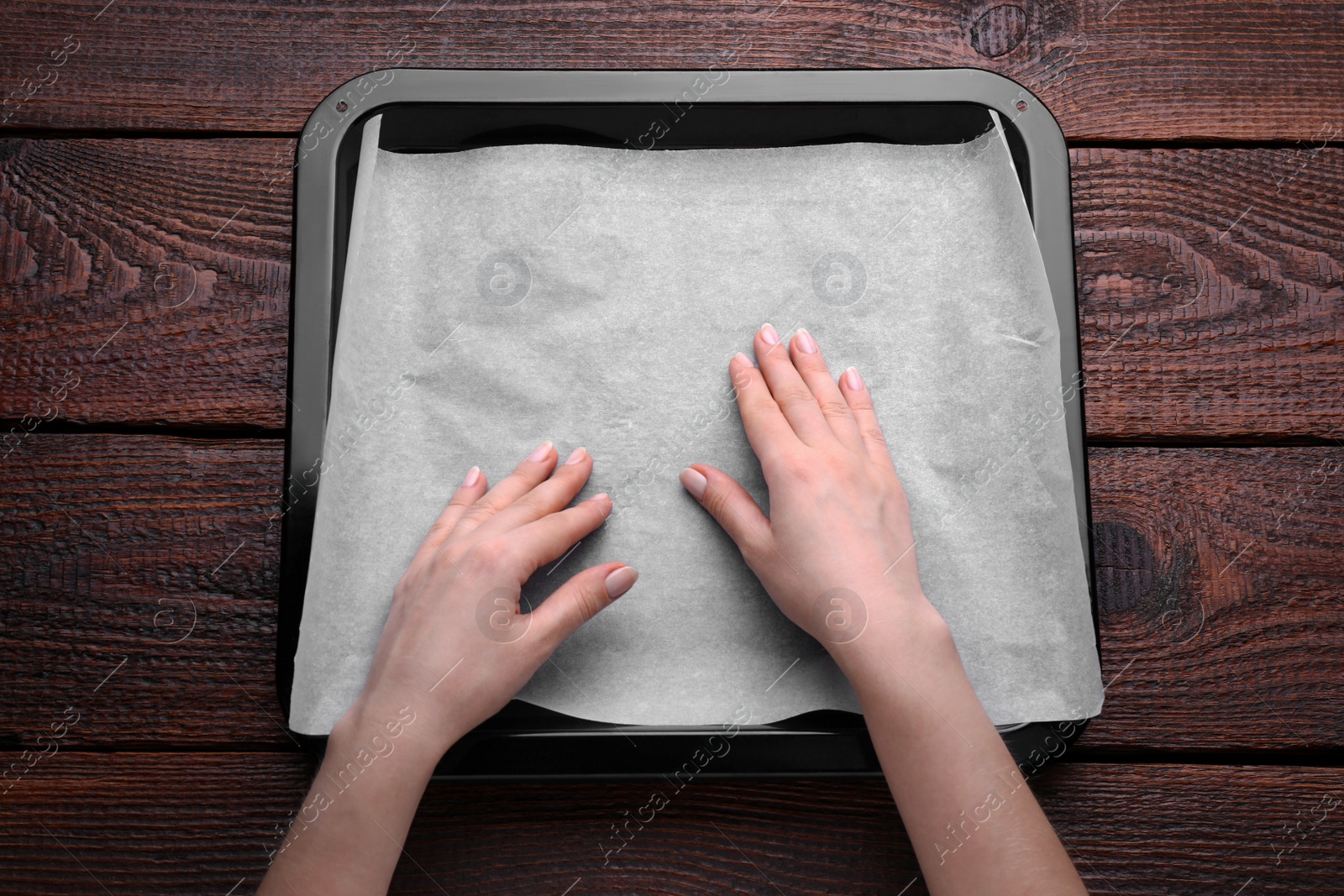 Photo of Woman putting parchment paper in baking pan at wooden table