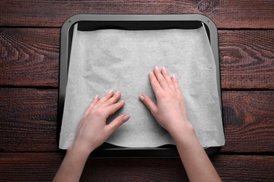 Woman putting parchment paper in baking pan at wooden table