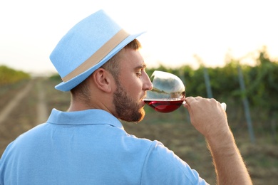 Photo of Young handsome man enjoying wine at vineyard on sunny day