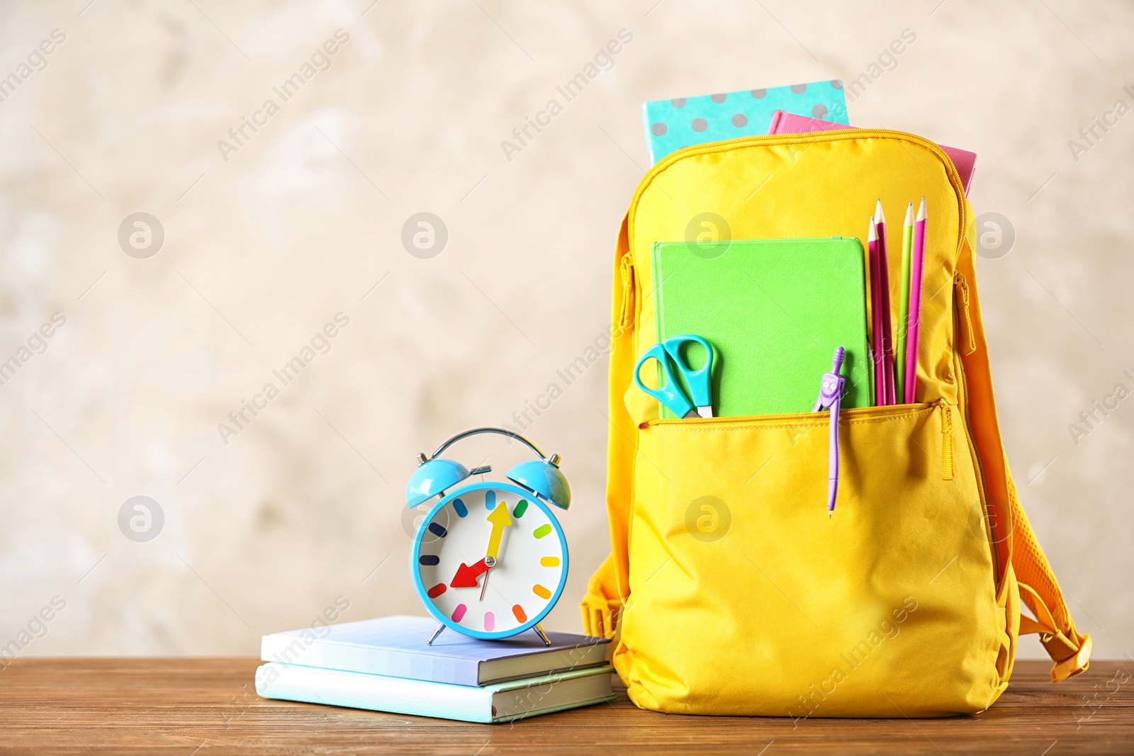 Photo of Backpack with school stationery on table against color background