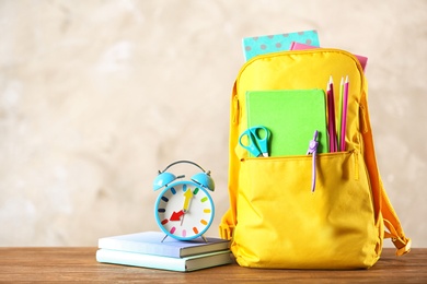 Photo of Backpack with school stationery on table against color background