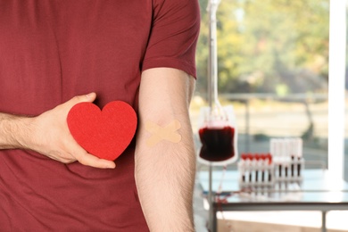 Photo of Man holding heart near hand with adhesive plasters at hospital, closeup. Blood donation concept