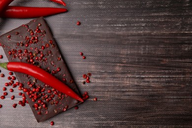 Photo of Delicious chocolate, fresh chili pepper and red peppercorns on wooden table, flat lay. Space for text