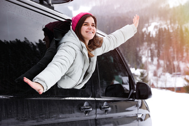 Happy young woman looking out of car window on road. Winter vacation
