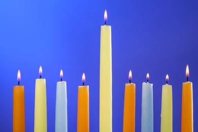 Photo of Hanukkah celebration. Colorful burning candles on blue background, closeup