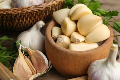 Photo of Fresh peeled garlic cloves in bowl and bulbs on wooden table, closeup. Organic product