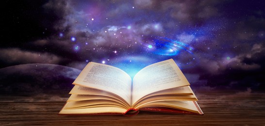Image of Wooden table with open book and beautiful universe on background