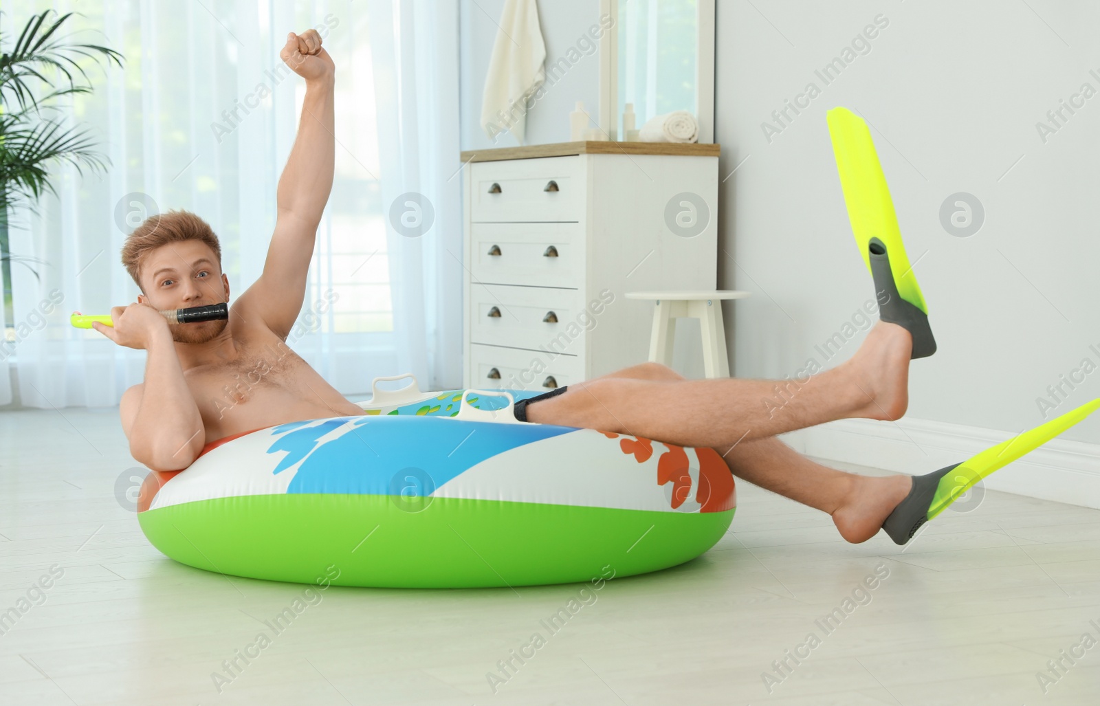 Photo of Handsome young man having fun with bright inflatable ring at home
