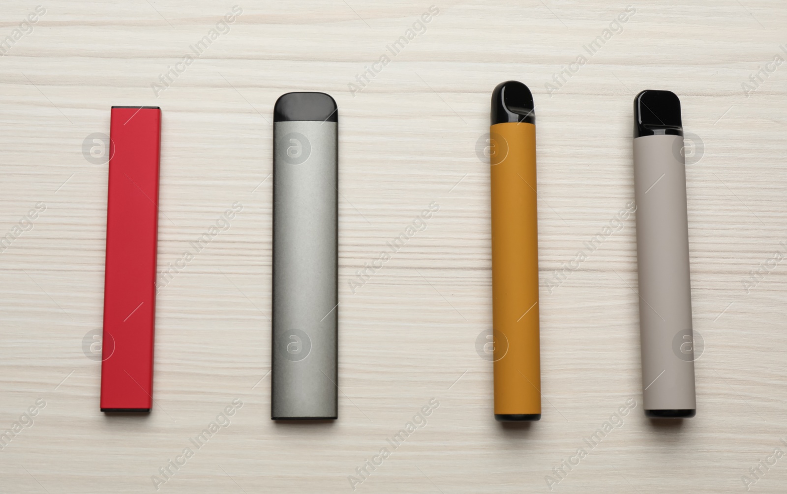 Photo of Different disposable electronic cigarettes on white wooden table, flat lay. Smoking alternative