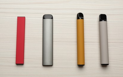 Photo of Different disposable electronic cigarettes on white wooden table, flat lay. Smoking alternative