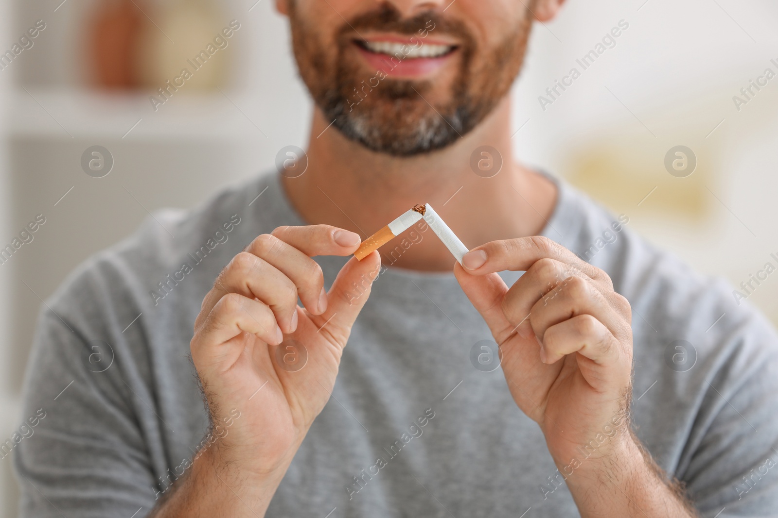 Photo of Stop smoking concept. Man breaking cigarette on blurred background, closeup