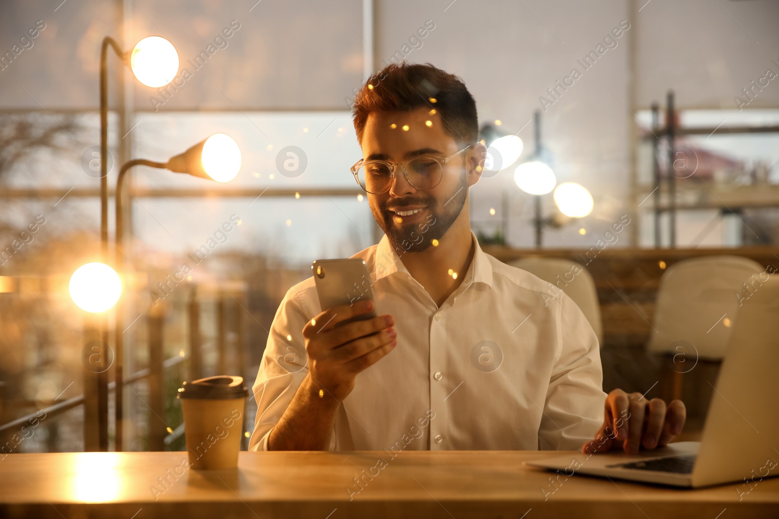 Photo of Man using smartphone while working with laptop in office