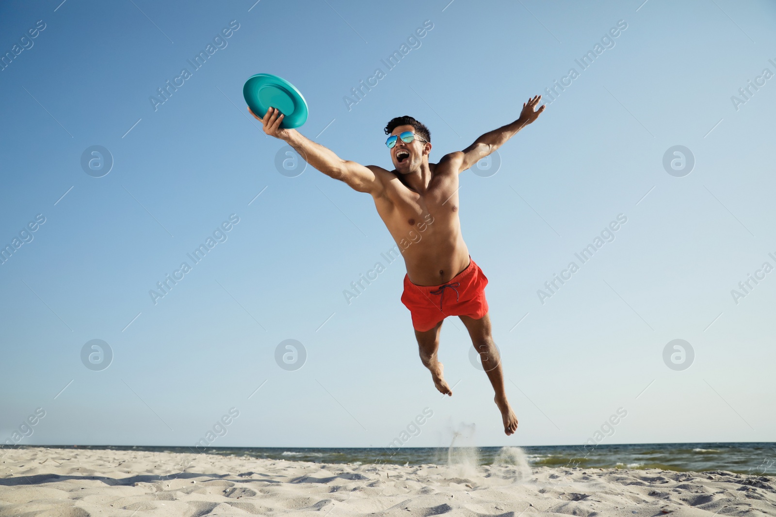 Photo of Sportive man jumping and catching flying disk at beach