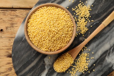 Photo of Millet groats in bowl and spoon on wooden table, flat lay