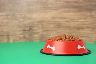 Photo of Dry dog food and feeding bowl on green table. Space for text