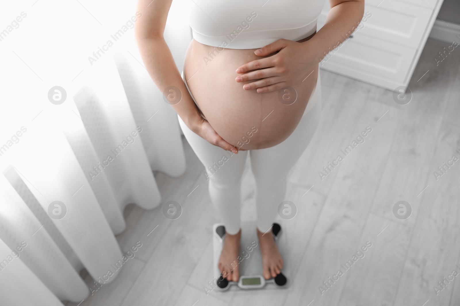 Photo of Pregnant woman standing on scales at home, closeup