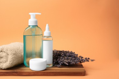 Photo of Cosmetic products, rolled towel and dry lavender flowers on orange background. Space for text