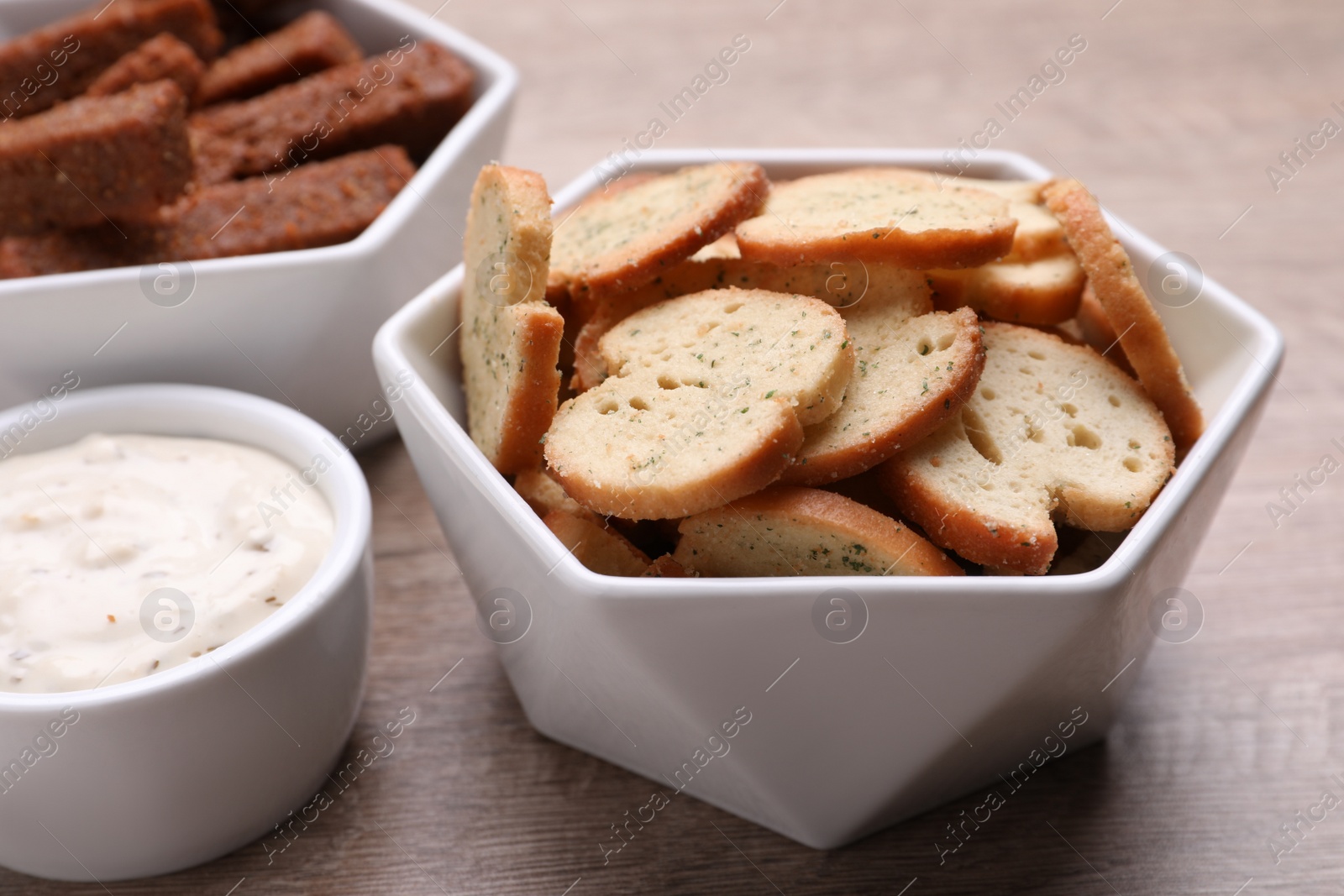 Photo of Different crispy rusks and dip sauce on wooden table, closeup
