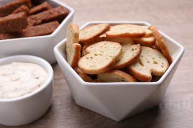 Different crispy rusks and dip sauce on wooden table, closeup