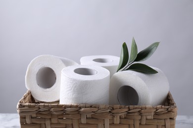 Photo of Toilet paper rolls and green leaves in wicker basket against light grey wall