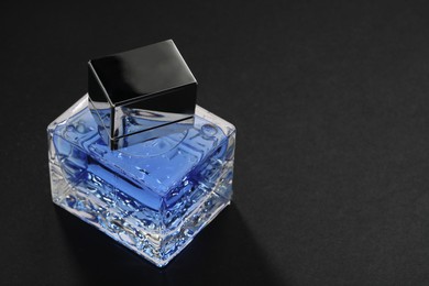 Blue men's perfume in bottle on black background, space for text