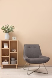 Photo of Living room interior with comfortable armchair and shelving unit near beige wall indoors